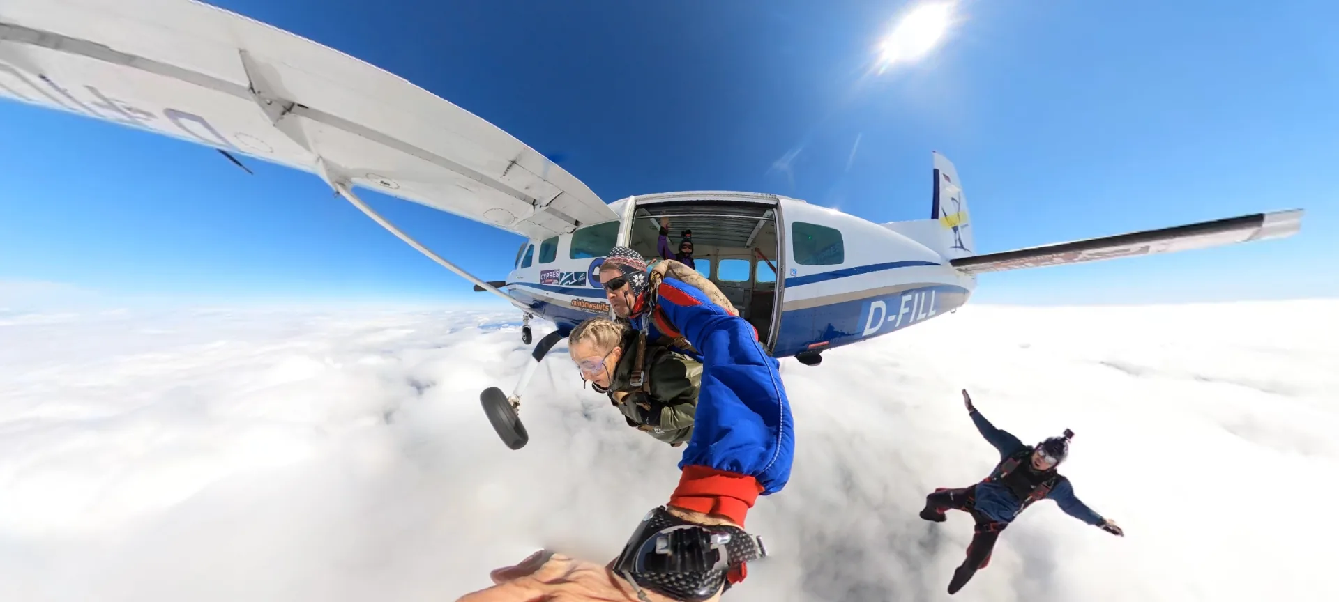 Professional tandem skydiving jump from aircraft showing instructor and client exiting plane over beautiful cloudy landscape